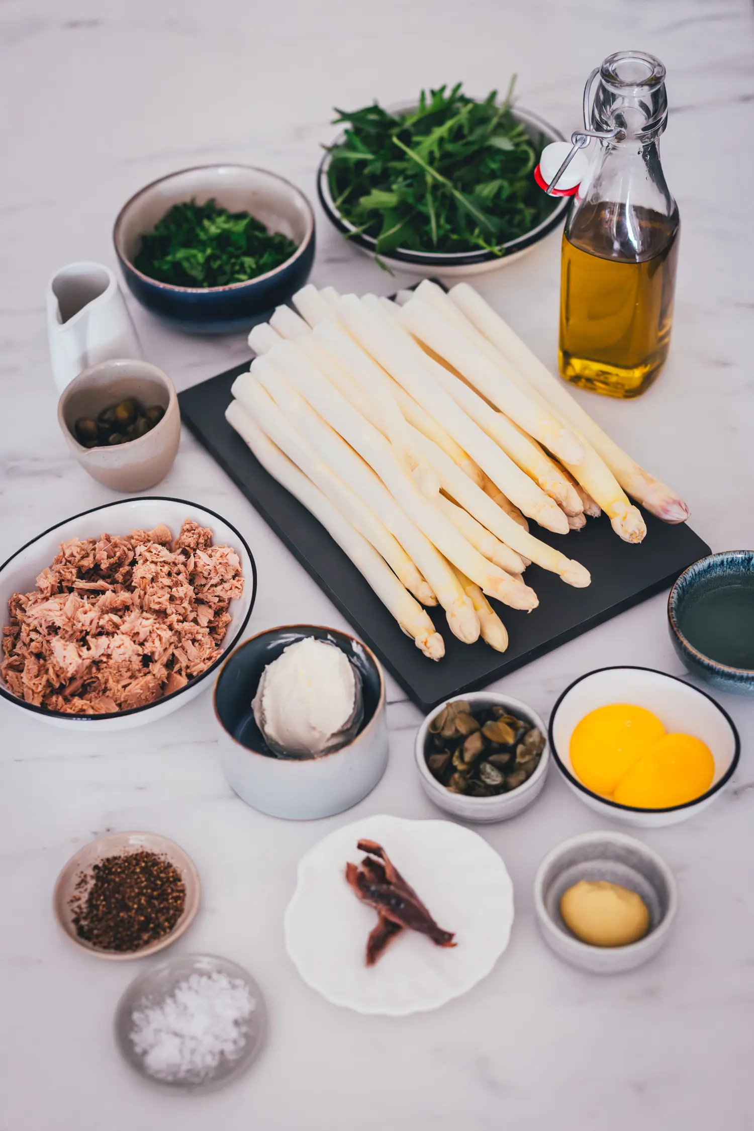 Zutaten für Spargel Tonnato in Schälchen angerichtet: weißer Spargel, Thunfisch in Öl, Sardellenfilets, Kapern, Eigelb, Olivenöl, Senf, Crème fraîche und Rucola