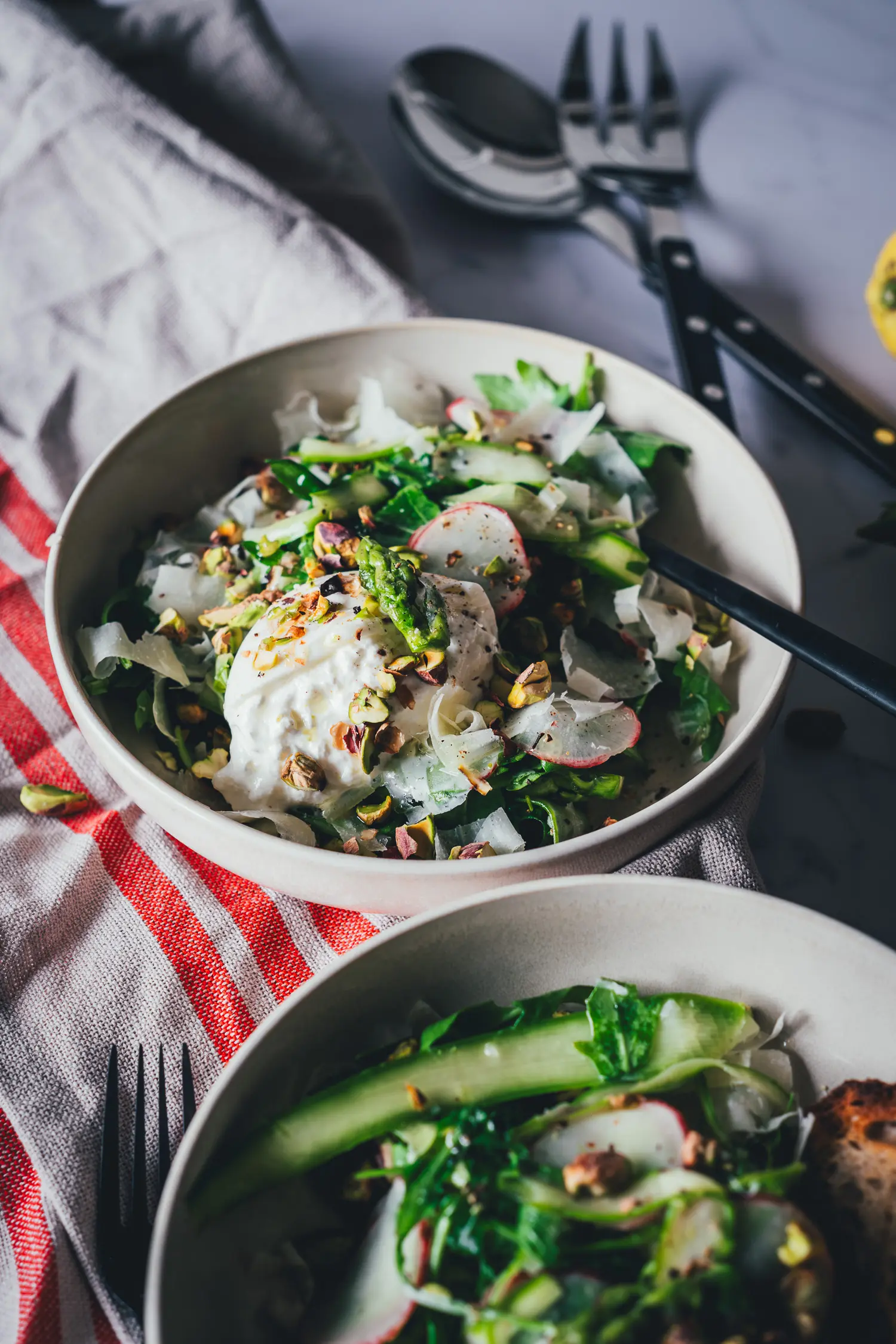 Nahaufnahme von rohem grünem Spargelsalat mit Burrata, Rucola, Radieschen und Parmesanspänen