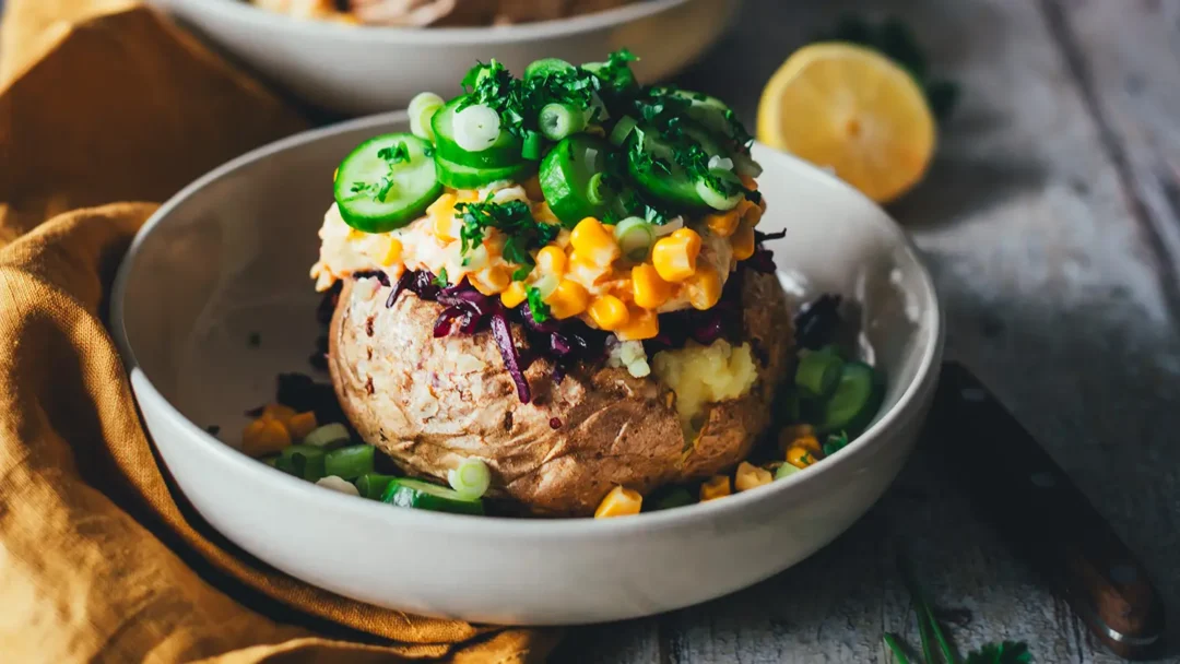 Kumpir-Backkartoffel aus dem Airfryer, getoppt mit Möhren-Joghurt, Mais, Gurkenscheiben und Rotkohlsalat, serviert in einer hellen Schale