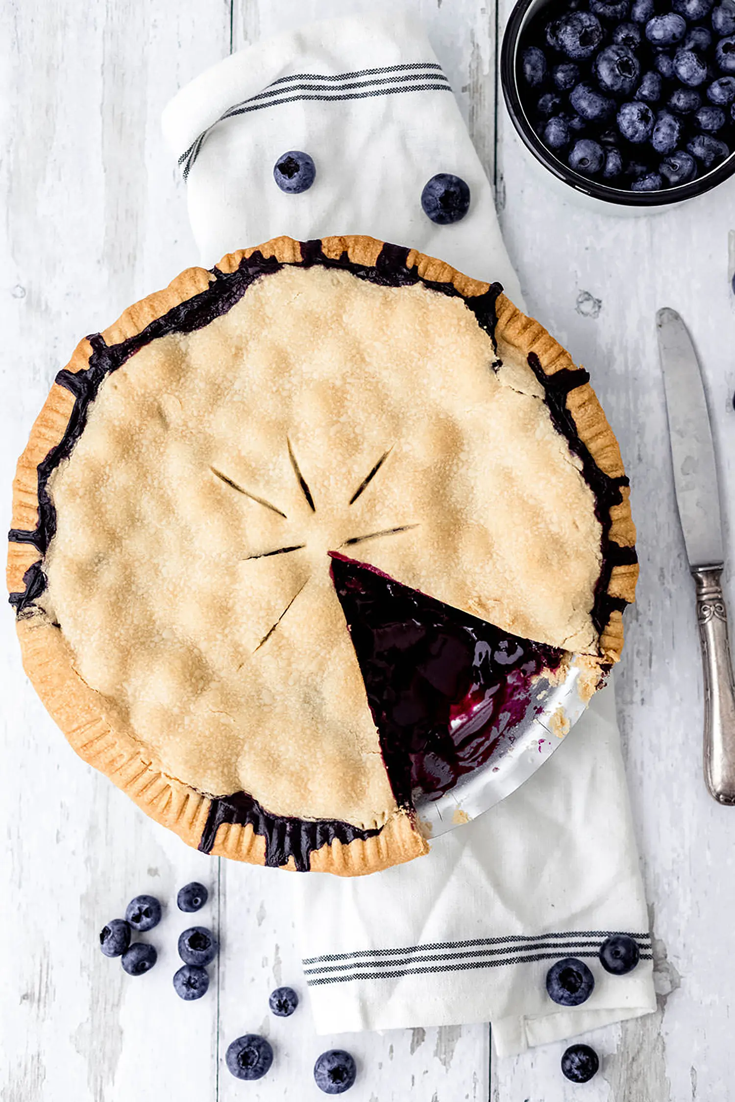 Topshot Aufnahme von einem frisch gebackenen und angeschnittenem Blueberry Pie mit frischen Blaubeeren