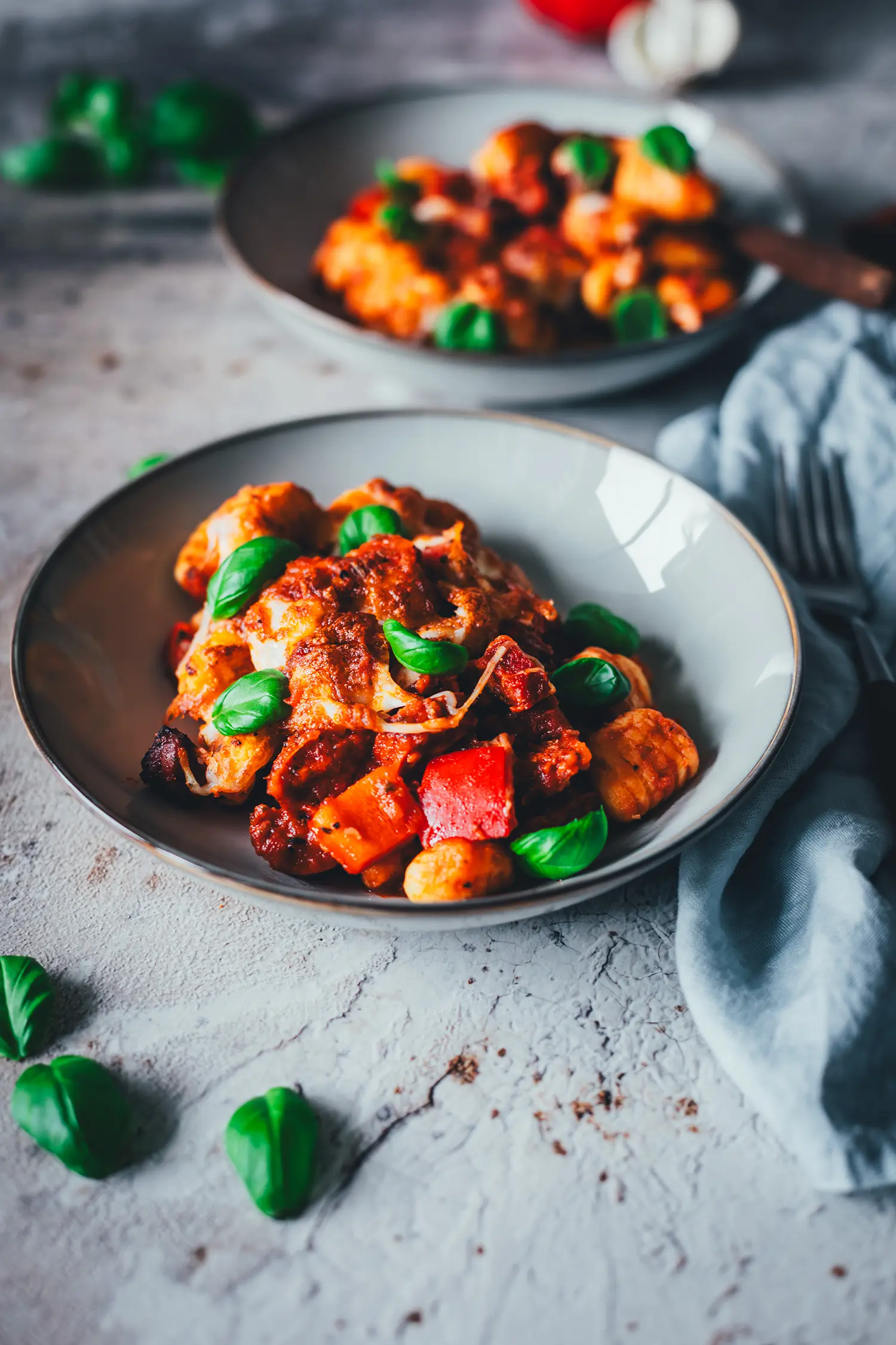 Nahaufnahme des Gnocchi-Auflaufs mit goldbrauner Mozzarella-Kruste, Tomatensauce und Basilikumblättern auf einem grauen Teller