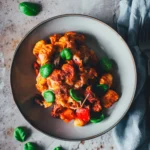 Überbackener Gnocchi-Auflauf mit Chorizo und Paprika in einer grauen Schale, von oben fotografiert und mit Basilikum bestreut