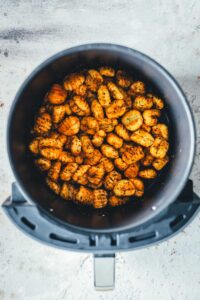 Gewürzte Gnocchi mit Paprikapulver und Kräutern im Korb der Heißluftfritteuse nach der ersten Garzeit