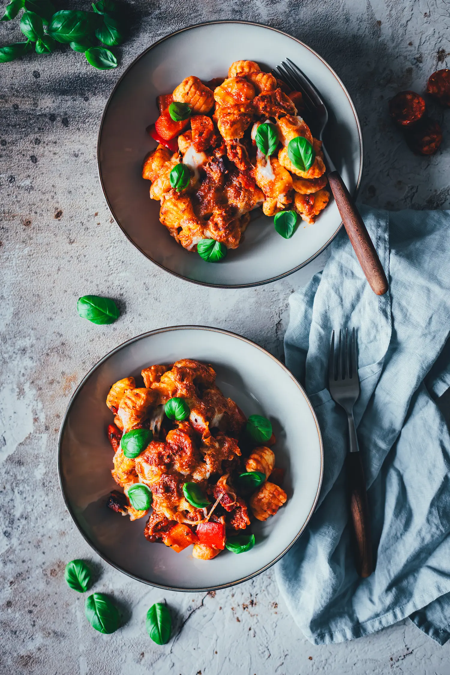Zwei Teller mit Gnocchi-Auflauf aus dem Airfryer von oben fotografiert, daneben Besteck, ein helles Leinentuch und einzelne Chorizoscheiben