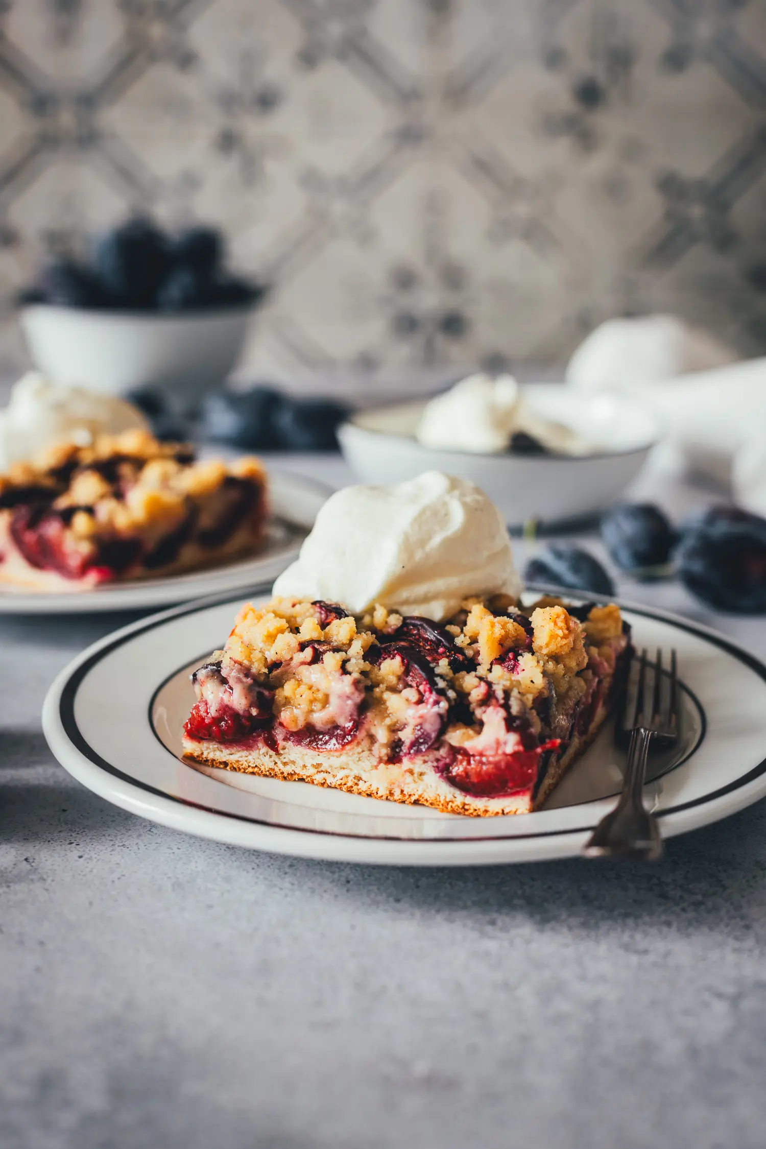 Nahaufnahme von zwei Stücken Zwetschgenkuchen auf weißen Tellern.