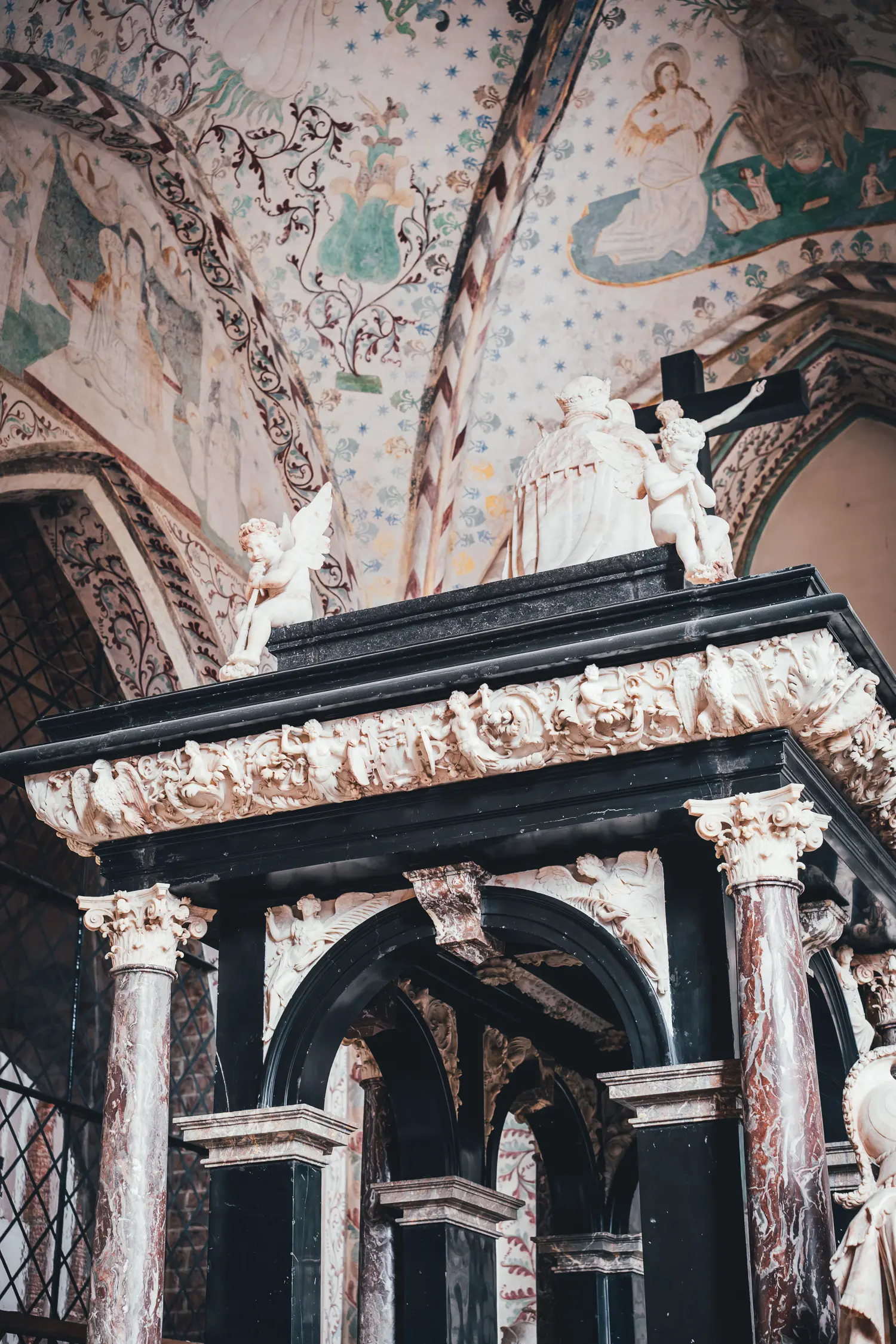 Grabmonument aus schwarzem Stein und rotem Marmor mit weißen Engelsfiguren und einer gekrönten Figur in einer Grabkapelle der Domkirke Roskilde, darüber ein Gewölbe mit Sternen und Ranken bemalt