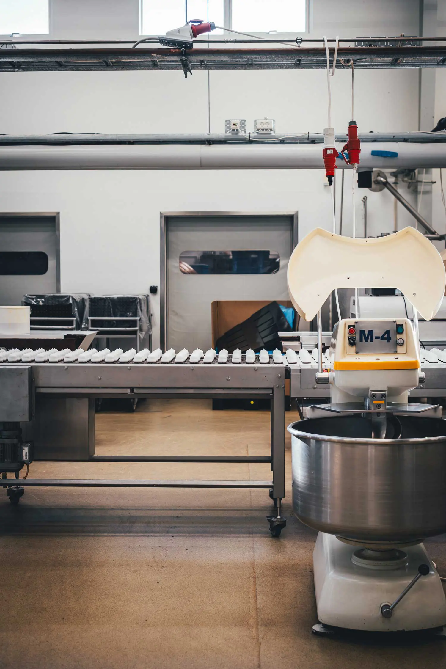 Reihen weißer Flødeboller auf einem Förderband in der Produktionshalle von Frellsen, daneben eine große Rührmaschine