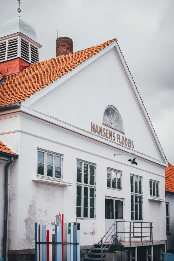 Weißer Giebel mit rotem Ziegeldach und dem Schriftzug Hansens Flødeis an der Fassade von Hansens Is in Jægerspris, davor eine Treppe mit Geländer