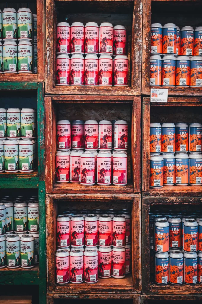 Holzregale im Hofladen des Herslev Bryghus mit Dosen in Reihen: grünes Landøl, rosa Rabarber Radler und orange-blaues alkoholfreies IPA
