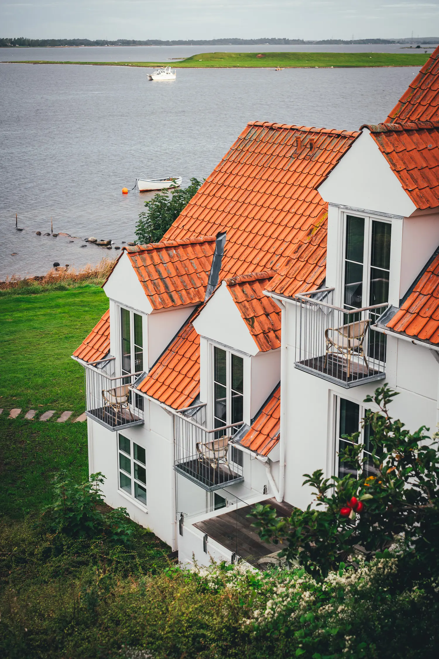 Weißes Gebäude des Hotels Søfryd mit roten Ziegeldächern und kleinen Balkonen, dahinter die Roskilde Fjord mit Booten