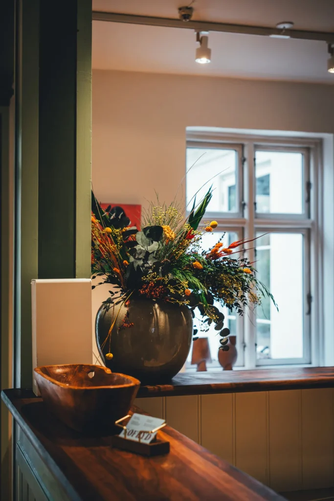 Trockenblumenstrauß in einer Vase auf dem Holztresen der Rezeption, daneben eine Holzschale und Visitenkarten