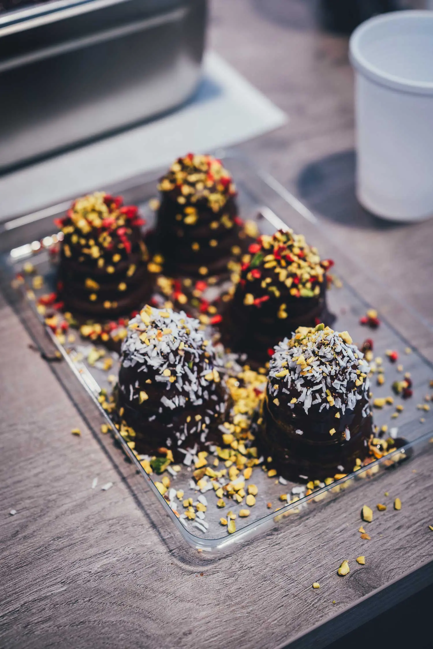Fünf fertige Flødeboller mit dunklem Schokoladenüberzug, bestreut mit Kokosraspeln, Pistazien und roten Beerenstückchen