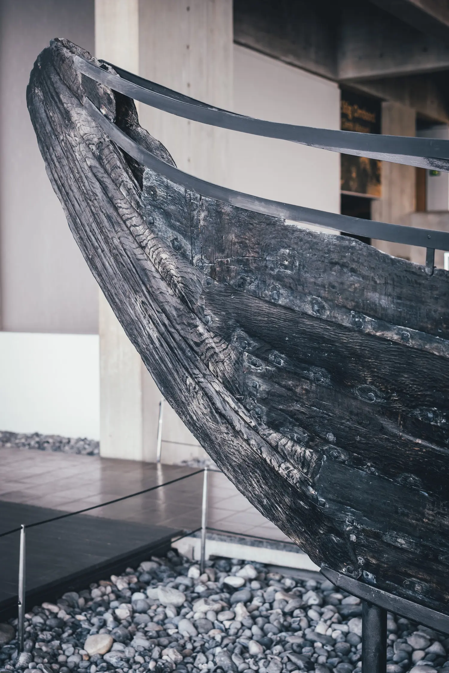 Dunkler, verwitterter Bug eines Wikingerschiffs aus dem 11. Jahrhundert auf Kieselsteinen in der Halle des Wikingerschiffmuseums Roskilde, das Holz wird von Metallstreben gehalten