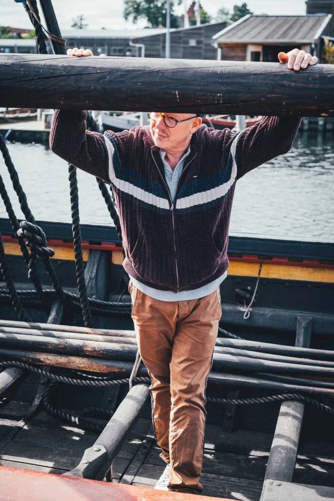 Torsten von Die Jungs kochen und backen steht an Bord eines Wikingerschiff-Nachbaus im Hafen des Wikingerschiffmuseums Roskilde und hält sich an der Rah über ihm fest
